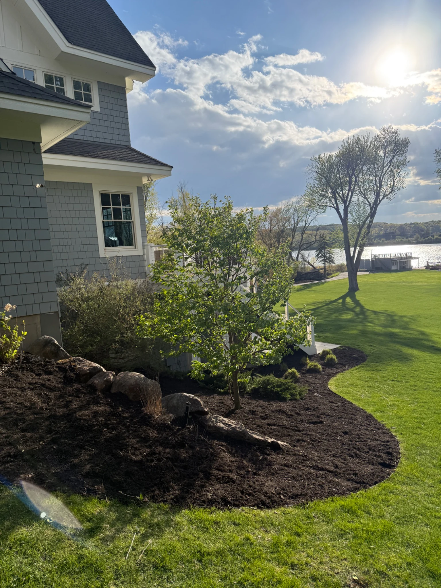 Finished landscape beds beside a lakeside home, with a sweeping lawn and lake views